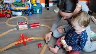 Image représentant la garde d'enfants  Une femme et un enfant jouant joyeusement avec un circuit de train en bois