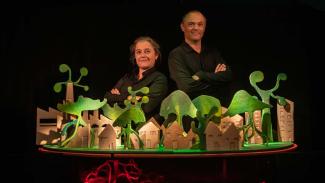 Spectacle nommé "L'arbre" à l'abbaye de Belleperche Deux personnes qui croisent les bras en regardant l'objectif avec devant eux une maquette avec des maisons et des arbres en cartons